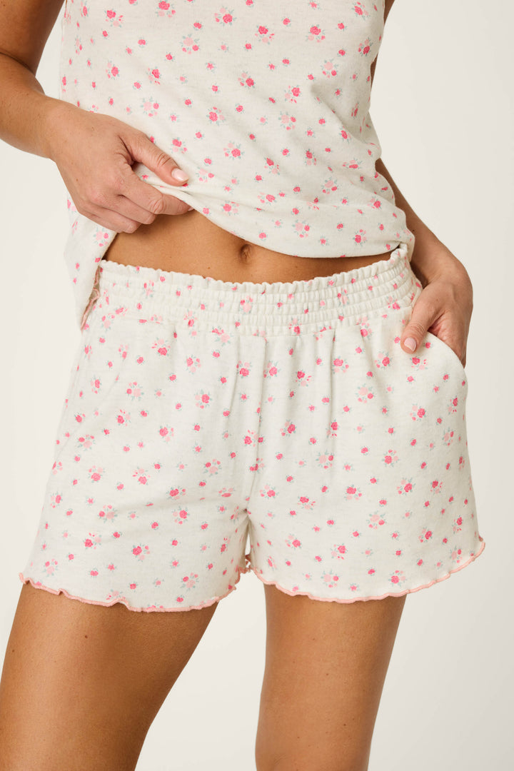 A person wearing the P.J. Salvage Romantic Rose Ditsy Rose Print Pajama Shorts with a matching top featuring small pink floral prints, one hand in the pocket and the other adjusting the waistband.