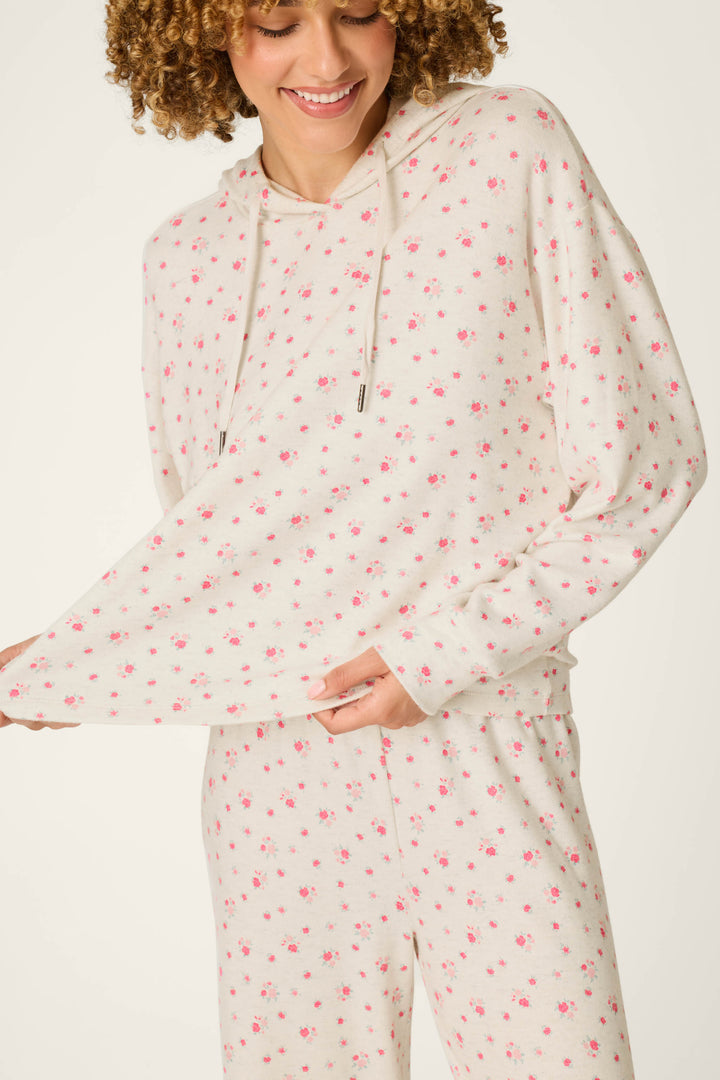 A person wearing the P.J. Salvage Romantic Rose Ditsy Rose Print Hoodie & Pants PJ Set, smiling and holding out the side of the cream-colored floral hoodie.