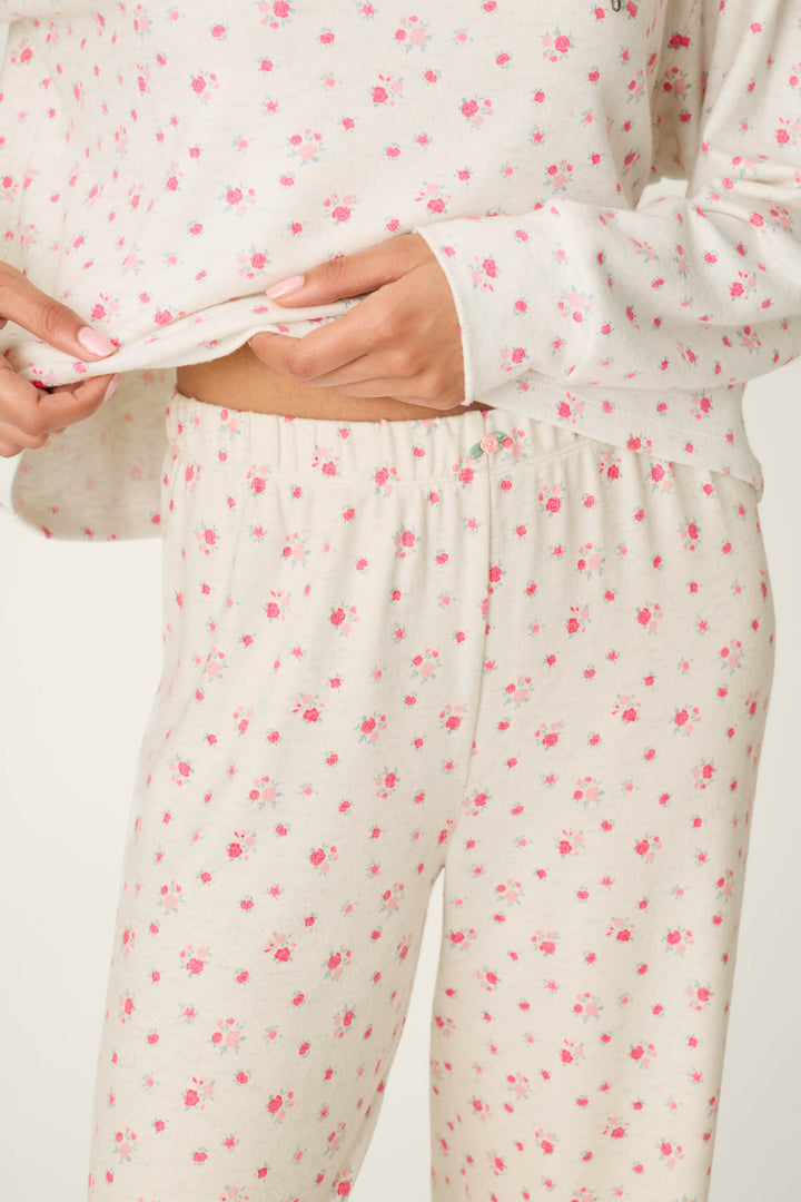 A person wearing the P.J. Salvage Romantic Rose Ditsy Rose Print Hoodie & Pants PJ Set holds the edge of their top, revealing the matching pants. The image focuses on their torso and hands.