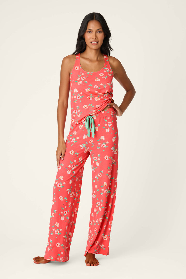 A woman stands barefoot in P.J. Salvage's Siesta Dreams Dark Coral Floral Print Pajama Pants, crafted from soft modal jersey with white florals and a comfy drawstring waist, paired with a matching sleeveless tank top.