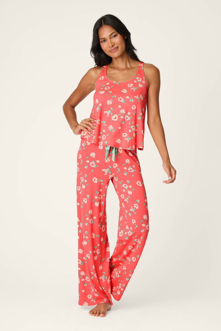 A woman stands barefoot in the P.J. Salvage Siesta Dreams Dark Coral Floral Print Long PJ Set, featuring wide-leg pants—ideal soft, breathable loungewear—posing against a plain light background.