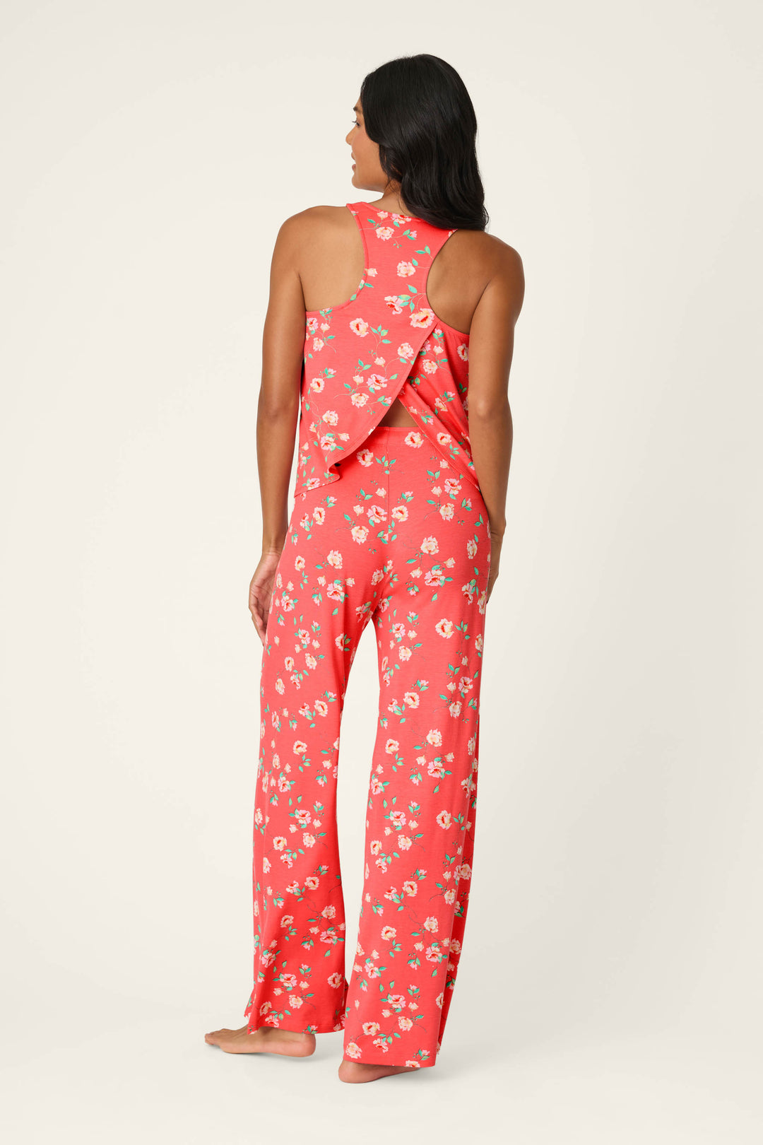 A woman with loose dark hair stands barefoot against a light background, wearing the Siesta Dreams Dark Coral Floral Print Long PJ Set by P.J. Salvage, effortlessly showcasing soft and breathable loungewear.