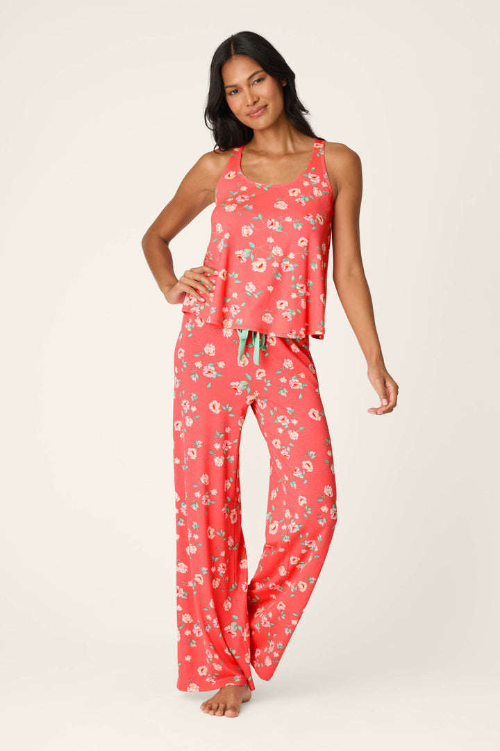 A woman wearing the P.J. Salvage Siesta Dreams Dark Coral Floral Print Tank Top stands smiling with one hand on her hip against a plain light background, paired with wide-leg pajama pants in soft modal jersey.