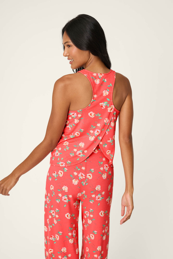 A woman with long dark hair wears the P.J. Salvage Siesta Dreams Dark Coral Floral Print Tank Top, featuring a sleeveless design and floral pattern, as she looks over her shoulder and smiles against a neutral background.