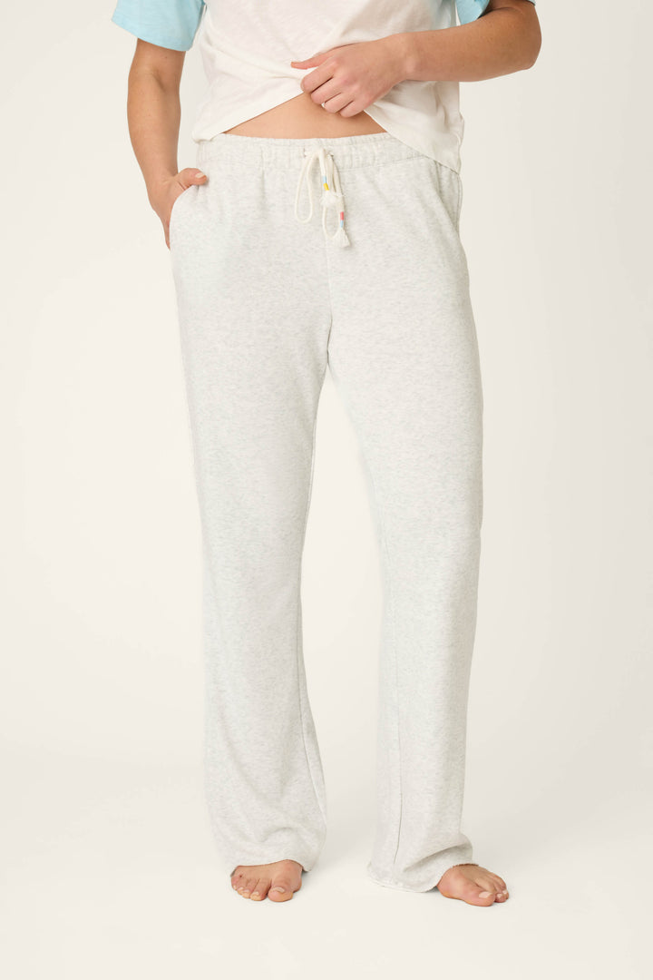A person stands barefoot on a plain background, wearing P.J. Salvage Sunday Funday Open Leg Lounge Pants in light gray and a short-sleeve shirt, with one hand in the pocket and the shirt slightly lifted to show the waistband.