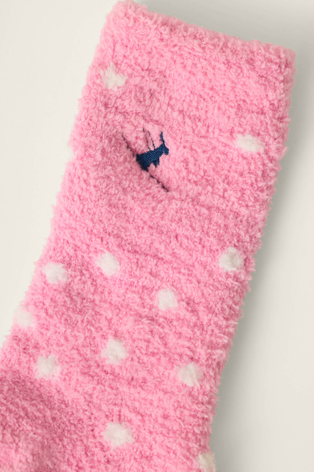 A close-up of the P.J. Salvage Ski Jammie Classics Ski Bunny & Snowflakes Socks, featuring soft pink fabric with white polka dots and a small embroidered blue bunny near the top.