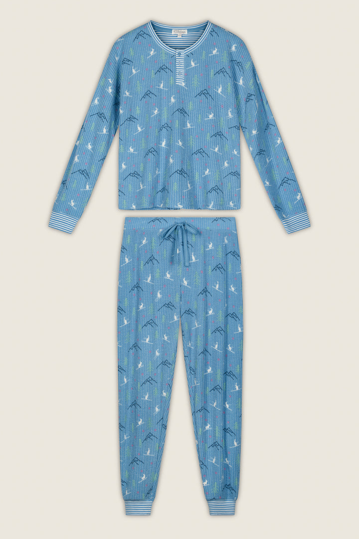 The P.J. Salvage Ski Jammie Classics Skiing Bunnies Long Sleeve Jogger PJ Set features a blue long-sleeve design with a drawstring waist, vertical stripes, and a playful print of clouds and mountain shapes. The cuffs are detailed with horizontal white and blue stripes.
