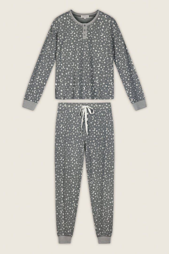 The P.J. Salvage Ski Jammie Classics Celestial Print Long Sleeve Jogger PJ Set is displayed laid flat on a light background, featuring gray fabric with white celestial patterns, striped cuffs, and a drawstring waistband.