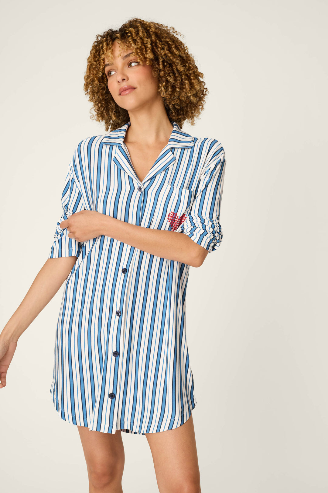 A person with curly hair wears the P.J. Salvage Soiree Dreams Blue Stripe Nightshirt, sleeves rolled up, looking to the side in a relaxed pose against a plain light background.