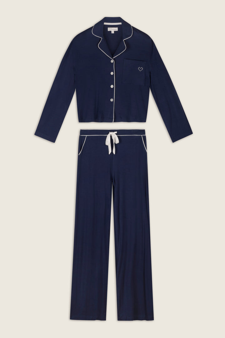 The Soiree Dreams Deep Navy Long Sleeve PJ Set by P.J. Salvage, featuring white piping, includes a button-up top with a front pocket and matching drawstring pants, displayed flat on a light background.
