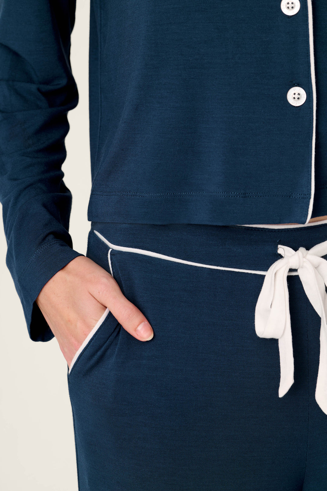 Model wearing the Soiree Dreams Deep Navy Long Sleeve PJ Set by P.J. Salvage, featuring white trim and a drawstring waist, with one hand in the pocket, shown from shoulders to thighs against a light background.