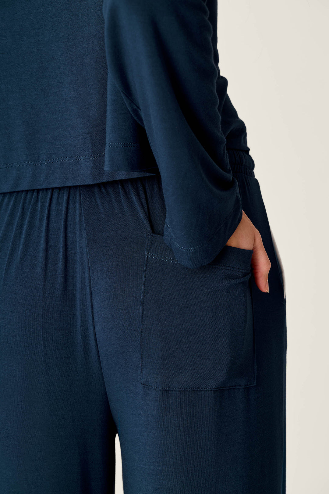 A person wearing the Soiree Dreams Deep Navy Long Sleeve PJ Set by P.J. Salvage stands with their hand in a pocket. The image focuses on the side of their body, highlighting the top and pants with an elastic waistband and a visible pocket.