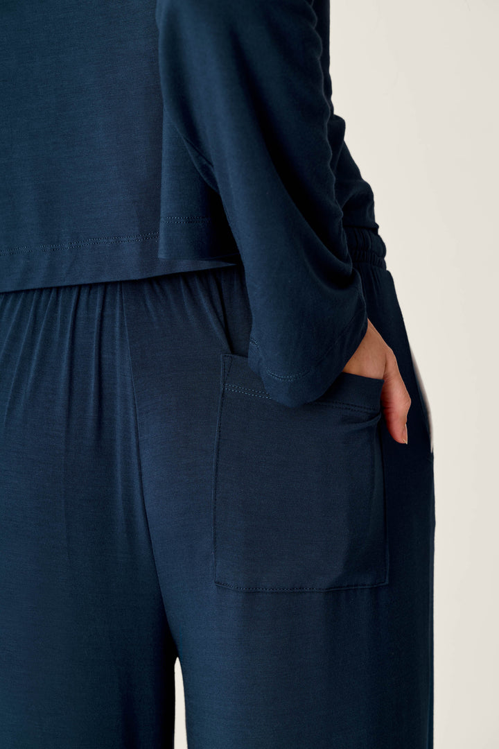 A person wearing the Soiree Dreams Deep Navy Long Sleeve PJ Set by P.J. Salvage stands with their hand in a pocket. The image focuses on the side of their body, highlighting the top and pants with an elastic waistband and a visible pocket.