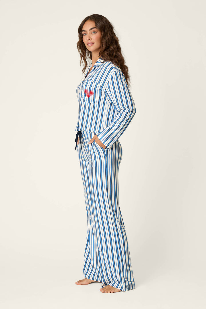 A woman stands sideways, barefoot on a plain light background, wearing the P.J. Salvage Soiree Dreams Blue Stripe Long Sleeve PJ Set.