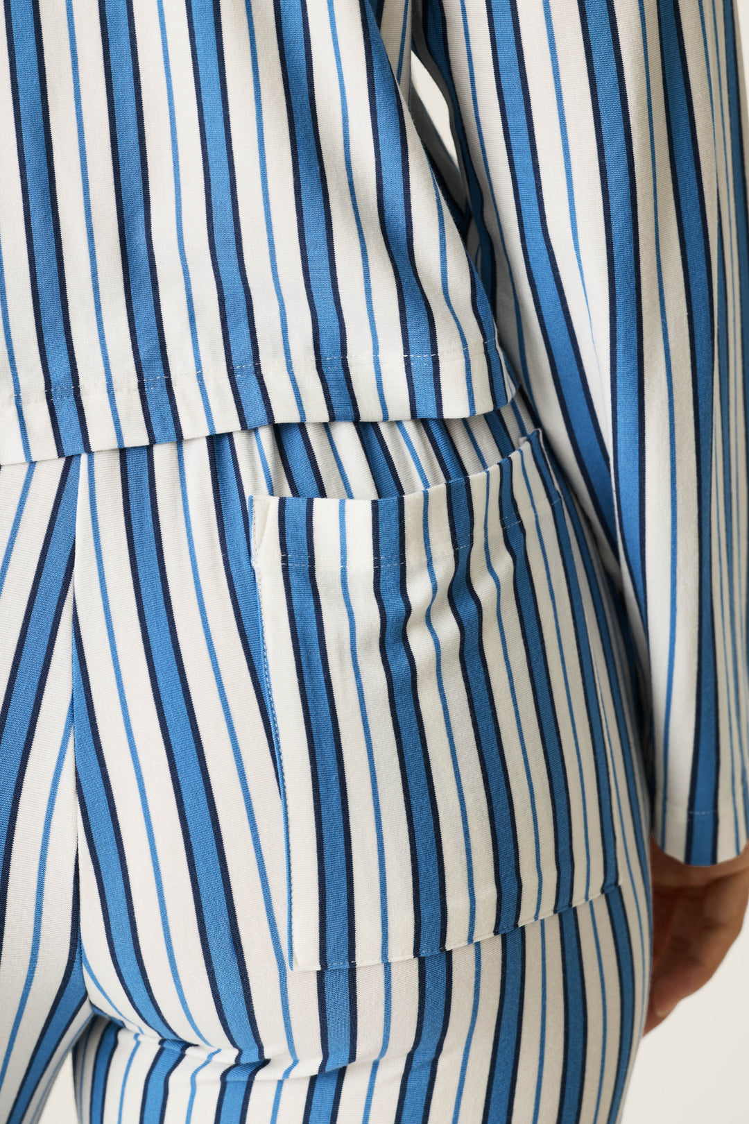 A close-up of a person wearing the P.J. Salvage Soiree Dreams Blue Stripe Long Sleeve PJ Set, featuring blue and white vertical stripes, highlighting the lower back, arm, hip, and a pocket on the pants.