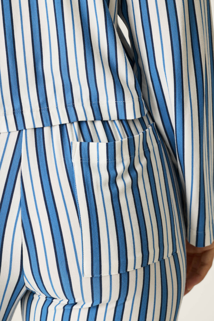 A close-up of a person wearing the P.J. Salvage Soiree Dreams Blue Stripe Long Sleeve PJ Set, featuring blue and white vertical stripes, highlighting the lower back, arm, hip, and a pocket on the pants.
