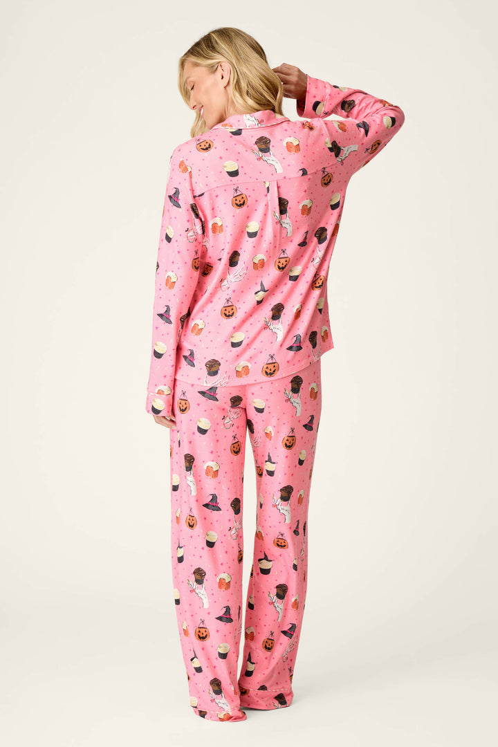 A person stands facing away, wearing the P.J. Salvage Sweet and Spooky Halloween Print Long Sleeve PJ Set, which features a playful pink design with pumpkins, witches, and candy on a light background. Their hand rests on the back of their head.
