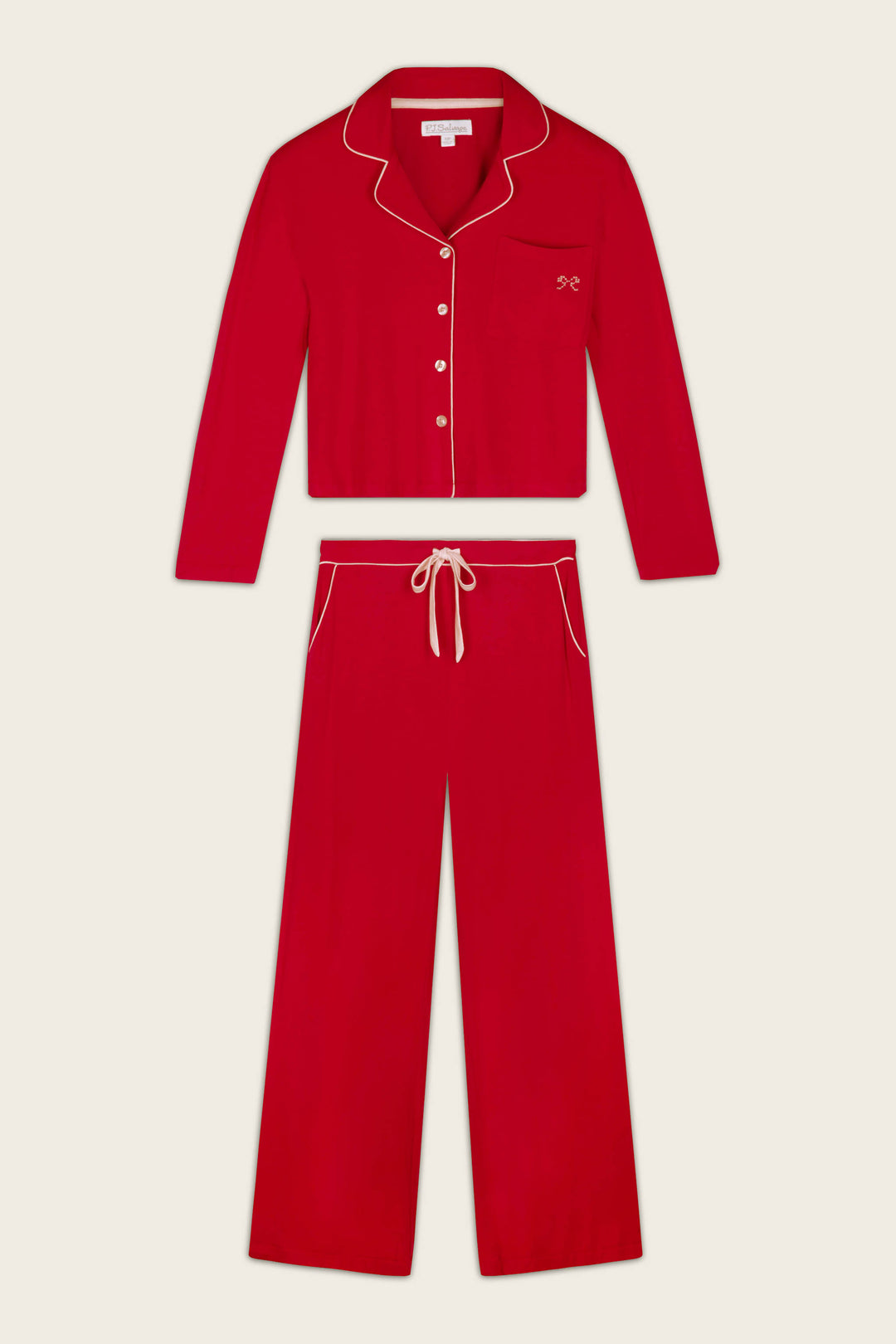 A two-piece red pajama set with cream-colored piping and trim, consisting of a long-sleeve button-front top with a collar, that has a bow embroidered on the chest pocket, and matching drawstring pants, displayed flat against a light beige background.