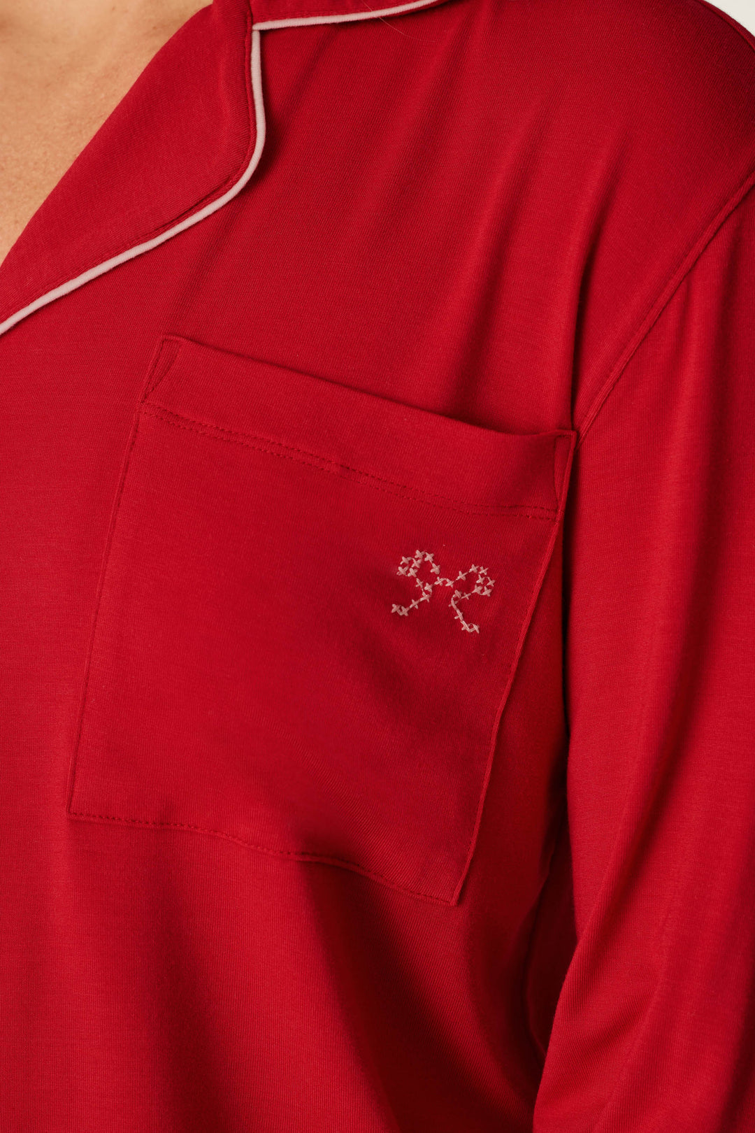 Close-up of the Sweetheart Dreams Red Long Sleeve PJ Set by P.J. Salvage, featuring a red pajama top with white piping along the collar and a front pocket adorned with a small white embroidered design near the top corner.