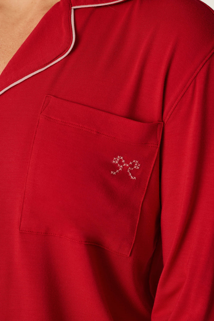 Close-up of the Sweetheart Dreams Red Long Sleeve PJ Set by P.J. Salvage, featuring a red pajama top with white piping along the collar and a front pocket adorned with a small white embroidered design near the top corner.