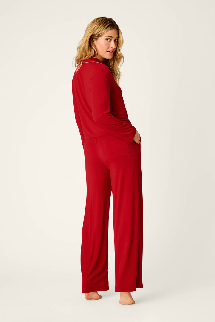 A woman stands barefoot against a plain light background, looking over her shoulder with one hand in her pocket, wearing the Sweetheart Dreams Red Long Sleeve PJ Set by P.J. Salvage.