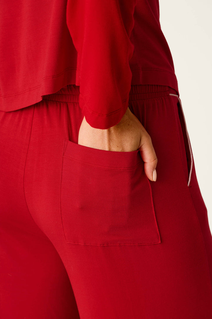 A person wearing the Sweetheart Dreams Red Long Sleeve PJ Set by P.J. Salvage places their right hand in the back pocket of the red pajama pants, with the focus on their lower back and hand while the rest of their body is out of frame.