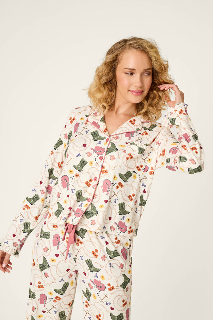 A person wearing the P.J. Salvage Saddle Up Western Print Long Sleeve Top stands against a plain light background, looking to the side and lightly touching their hair with a relaxed, pleasant expression.