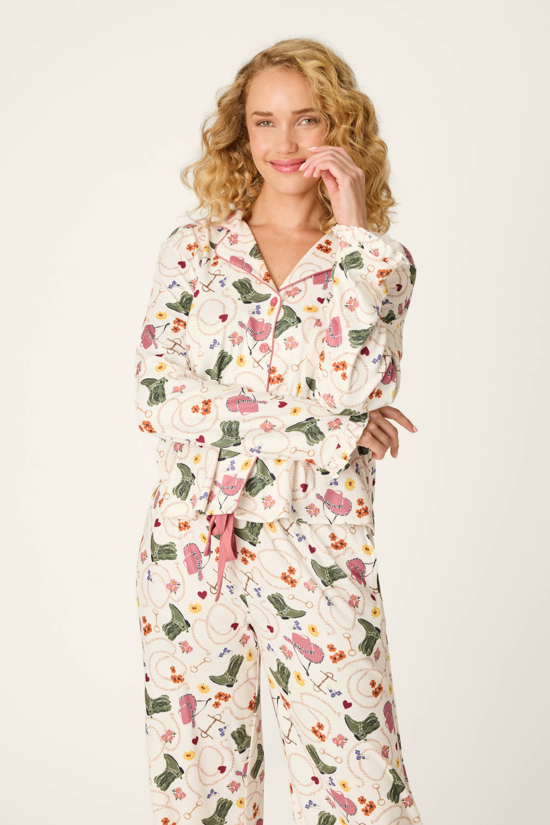 A person with curly blonde hair wears the P.J. Salvage Saddle Up Western Print Long Sleeve Top, smiling with one hand touching their face and the other arm crossed.