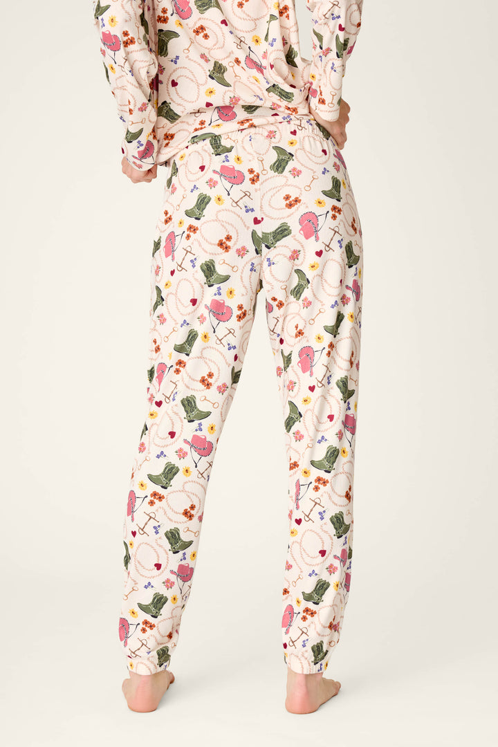 A person standing barefoot, shown from the back, wearing P.J. Salvage Saddle Up Western Print Pajama Jogger Pants featuring a colorful floral and leaf pattern.