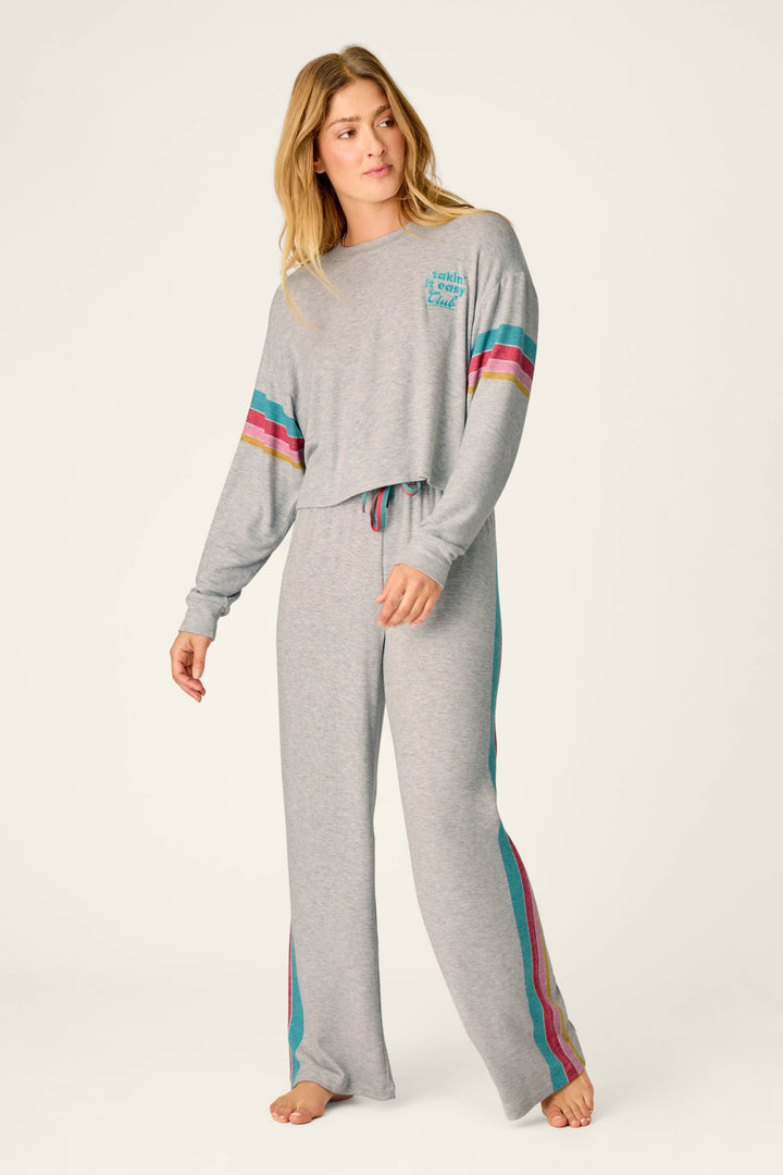 A woman wearing the P.J. Salvage Takin’ It Easy Club Striped Long Sleeve Top, featuring colorful stripes on the sleeves and pants, stands barefoot against a plain background.