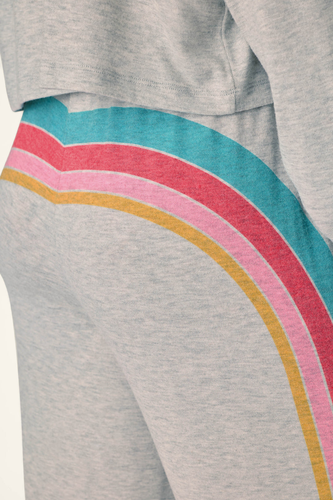 Close-up of a person wearing the P.J. Salvage Takin’ It Easy Club Striped Lounge Pants in light gray, featuring colorful rainbow stripes in teal, pink, red, and yellow down the side. The matching sweatshirt is partially visible at the top of the image.