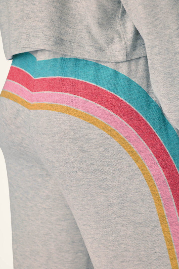 Close-up of a person wearing the P.J. Salvage Takin’ It Easy Club Striped Lounge Pants in light gray, featuring colorful rainbow stripes in teal, pink, red, and yellow down the side. The matching sweatshirt is partially visible at the top of the image.