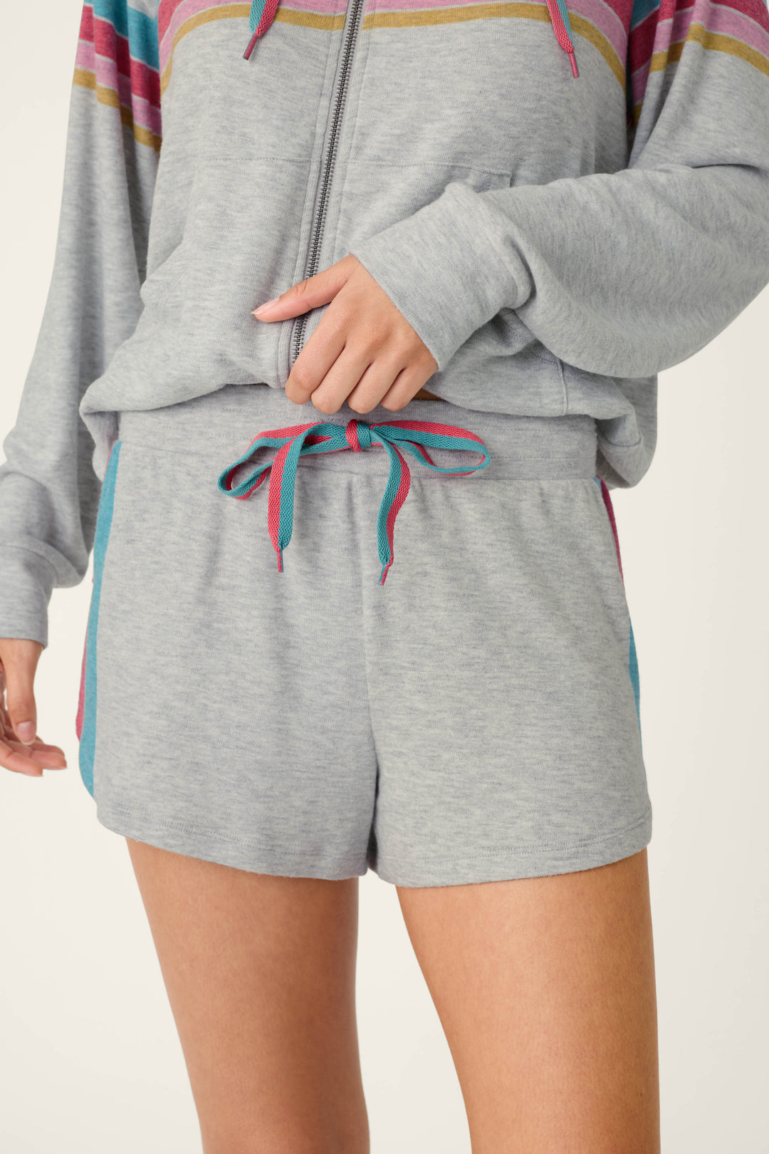 A person wearing the P.J. Salvage Takin’ It Easy Club Striped Shorts and a matching zip-up sweatshirt with colorful stripes on the chest and drawstring.