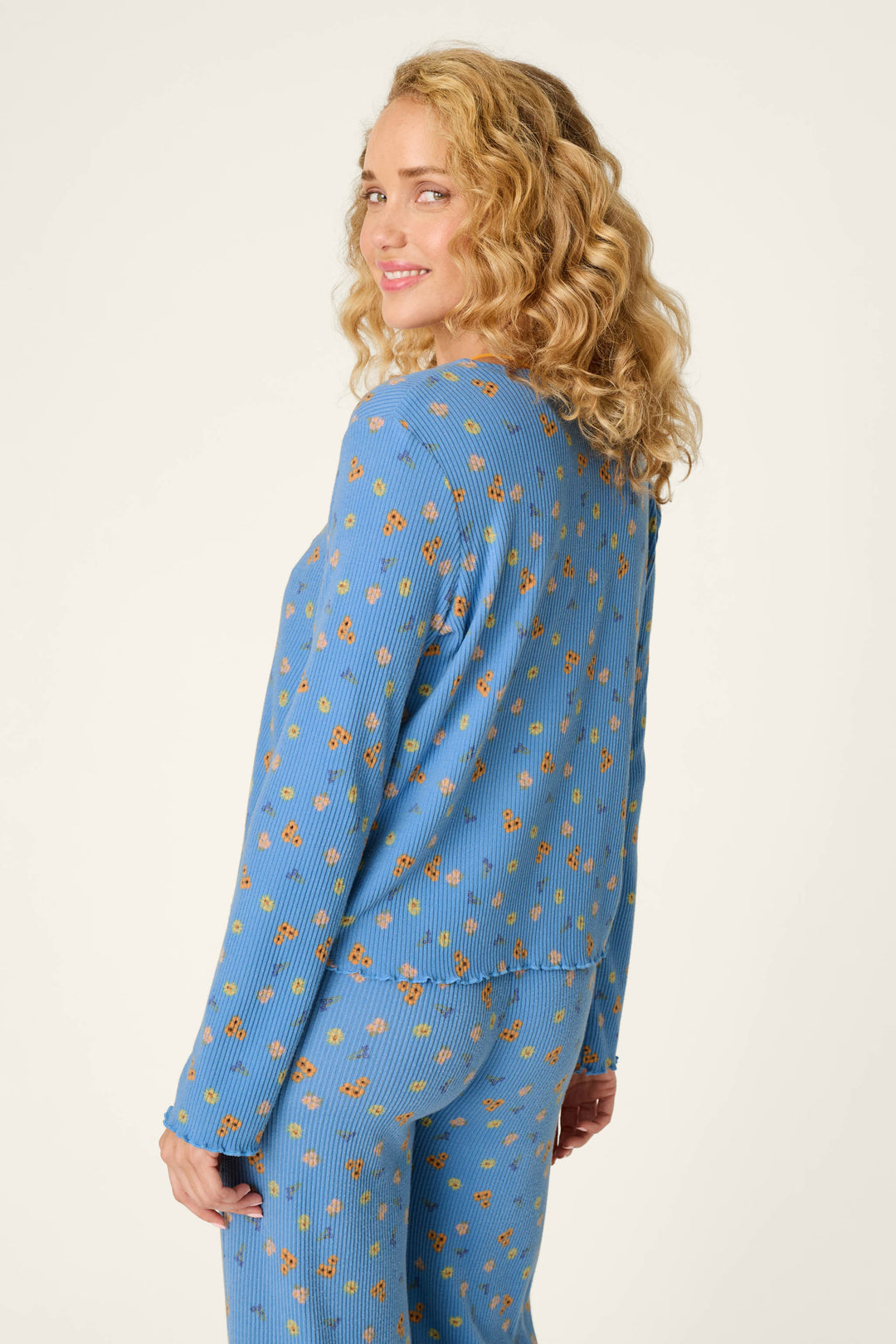 A woman with curly blonde hair smiles as she stands sideways, looking over her shoulder and wearing the P.J. Salvage Tiny Blooms Paris Blue Floral Print Tie-Front Top.