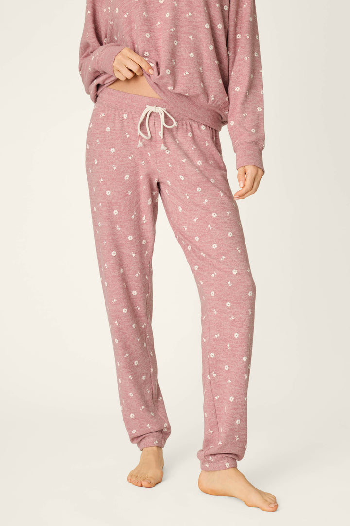 A person is wearing the P.J. Salvage Tiny Blooms Polka Dot Pajama Jogger Pants, featuring a light pink color with a white floral pattern and a drawstring waist. The image captures the body from the shoulders down, showing the individual standing barefoot against a light background.