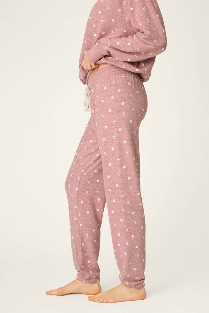 A person stands barefoot on a light background, wearing P.J. Salvage’s Tiny Blooms Polka Dot Pajama Jogger Pants and a matching long-sleeve top with small white floral patterns.
