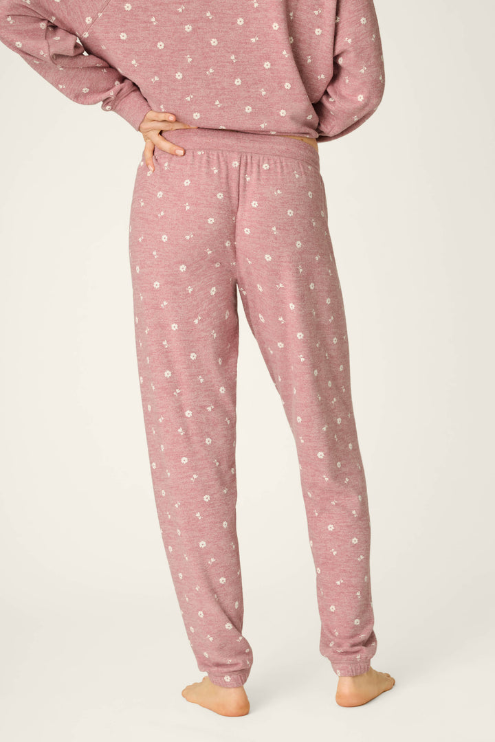 A person stands barefoot, facing away, with one hand on their hip, wearing the P.J. Salvage Tiny Blooms Polka Dot Pajama Jogger Pants in mauve with a small white floral print and a matching top. The background is plain and light-colored.