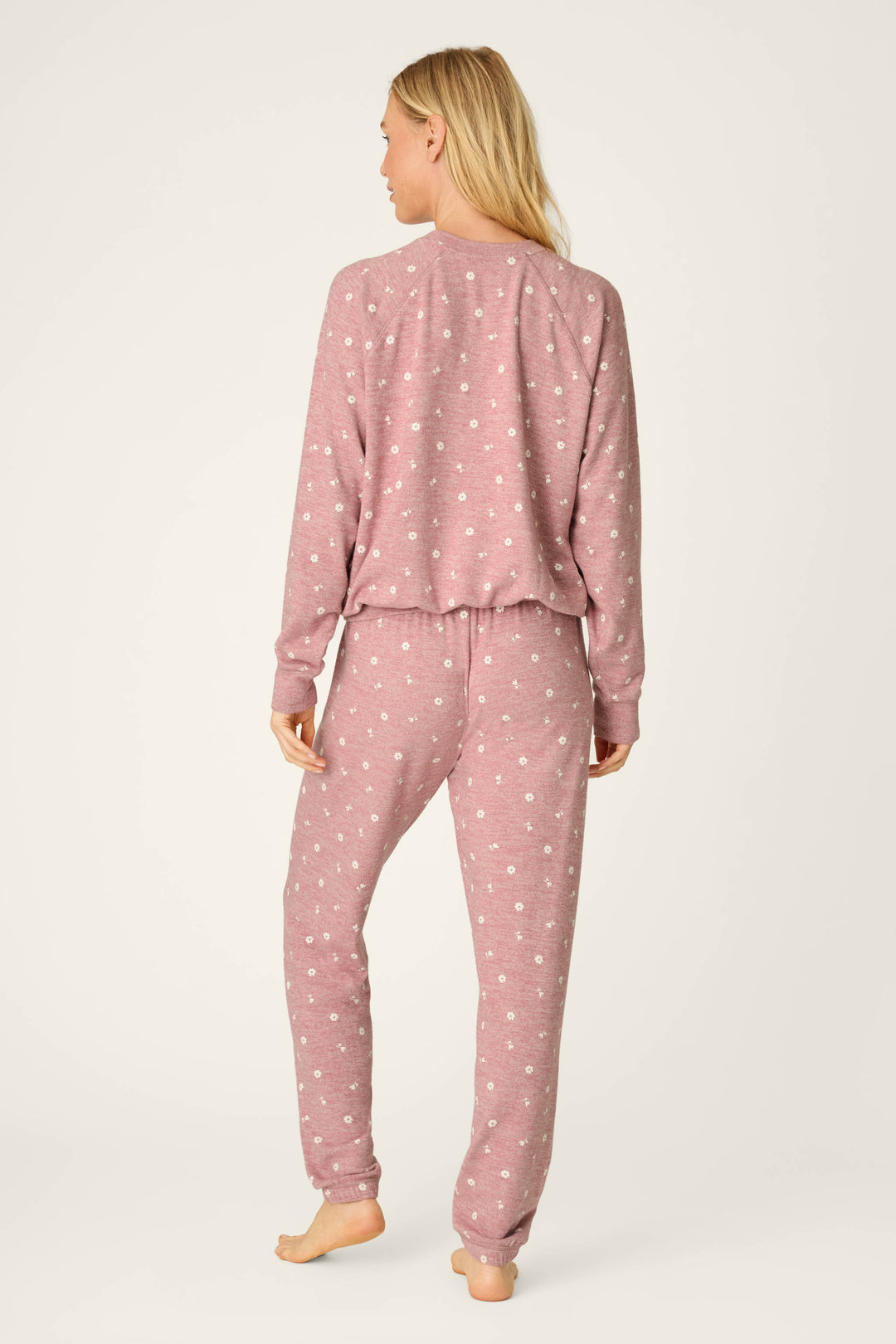 A person with long blonde hair is shown barefoot and facing away from the camera against a plain background, wearing the P.J. Salvage Tiny Blooms Polka Dot Long Sleeve PJ Set in pink with white polka dots.