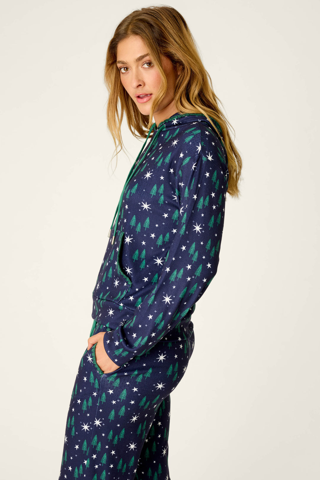 Wearing the P.J. Salvage “Under the Stars Magical Forest Print Hoodie,” a person with long hair stands sideways, hands in their pockets, looking toward the camera.