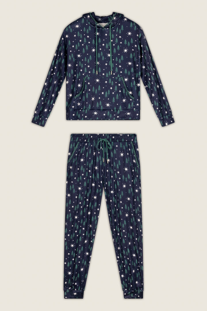 The Under the Stars Magical Forest Print Hoodie & Jogger Set by P.J. Salvage features a navy blue pajama set with a hoodie and pants, both adorned with a pattern of green Christmas trees and white stars.