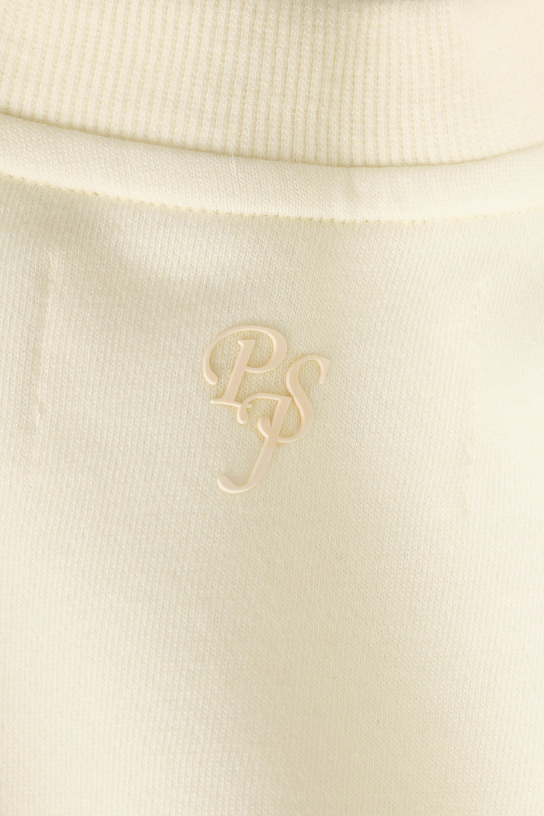 Close-up of a cream-colored ribbed fabric on the P.J. Salvage Western Ways Untamed Spirit Frankie Sweatshirt, featuring the overlapping letters “PS” embroidered or printed in a slightly glossy, matching cream color.