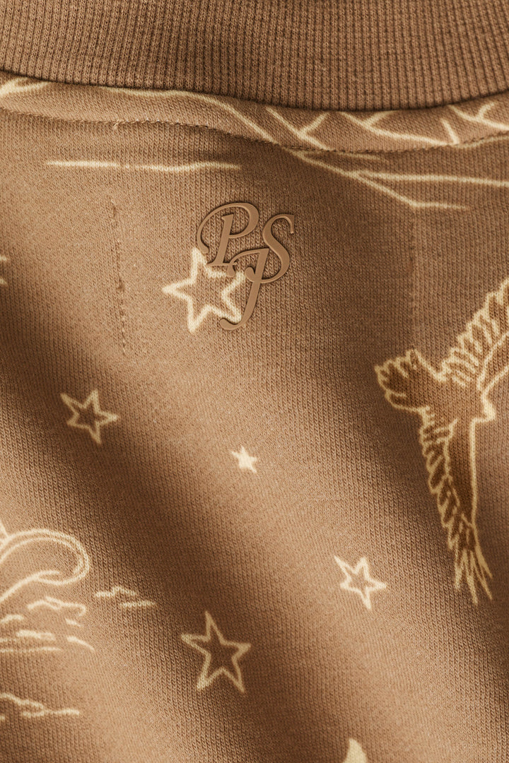 Close-up of the brown fabric of the P.J. Salvage Western Ways Ride ’Em Cowgirl Frankie Sweatshirt, featuring a subtle pattern of birds, stars, and lines, with an overlapping PS monogram at the center.