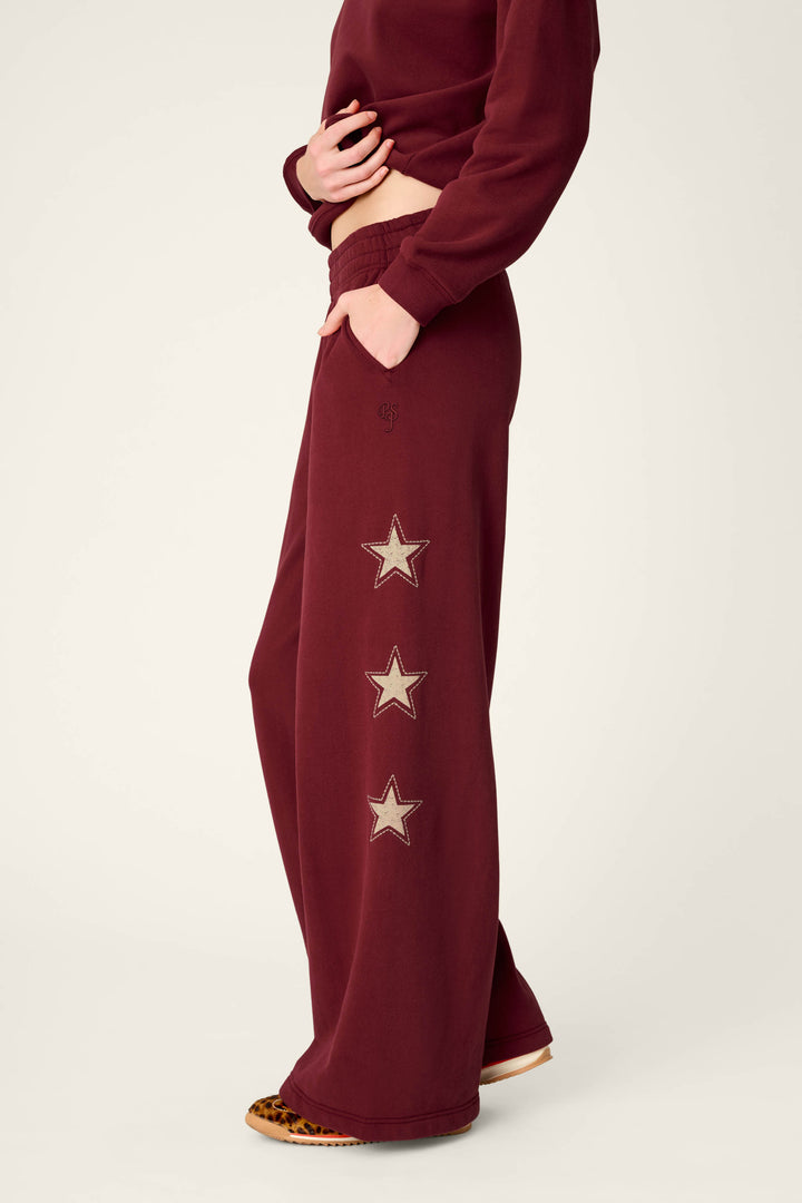 A person is wearing the P.J. Salvage Western Ways Dark Wine BFF Lounge Pants, featuring wide legs and three star patches on the side, paired with a matching burgundy sweatshirt and leopard print shoes. The person’s face is not visible.