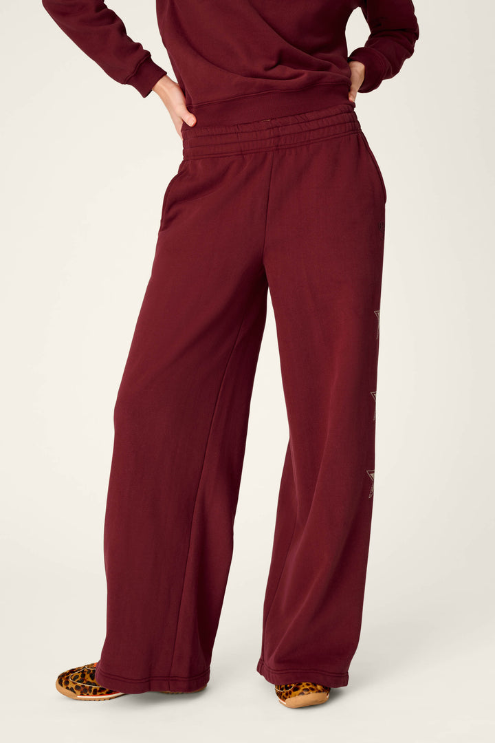 A person is shown from the waist down wearing P.J. Salvage’s Western Ways Dark Wine BFF Lounge Pants, paired with a matching top and leopard-print shoes. The background is plain off-white.