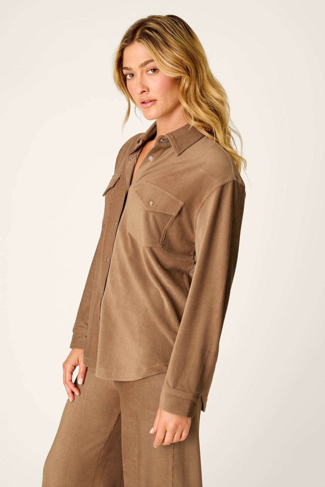 A person with long blonde hair wears the P.J. Salvage Western Ways Hey Cowboy Corduroy Knit Button Down Top in brown, featuring two chest pockets, paired with matching brown pants while standing against a plain light background.