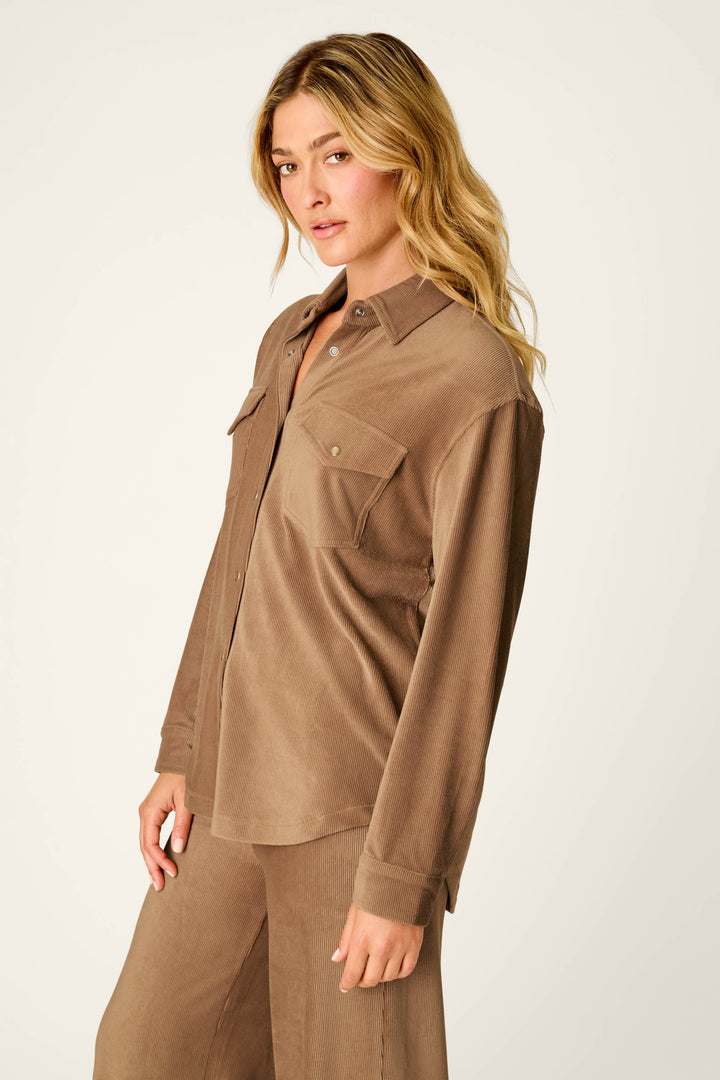 A person with long blonde hair wears the P.J. Salvage Western Ways Hey Cowboy Corduroy Knit Button Down Top in brown, featuring two chest pockets, paired with matching brown pants while standing against a plain light background.
