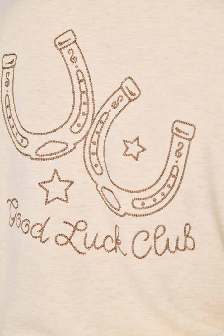 Two outlined horseshoes and two stars are positioned above the words “Good Luck Club,” written in cursive, on the light beige fabric of the P.J. Salvage Western Ways Good Luck Club Over Night Pullover.