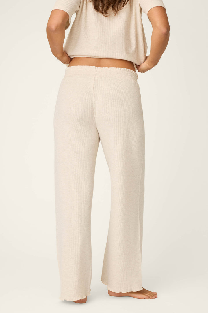 A person stands barefoot with their back to the camera, wearing P.J. Salvage Weekend Waffles Light Oatmeal Pajama Pants in a wide-leg silhouette and a matching short-sleeve top against a plain background.