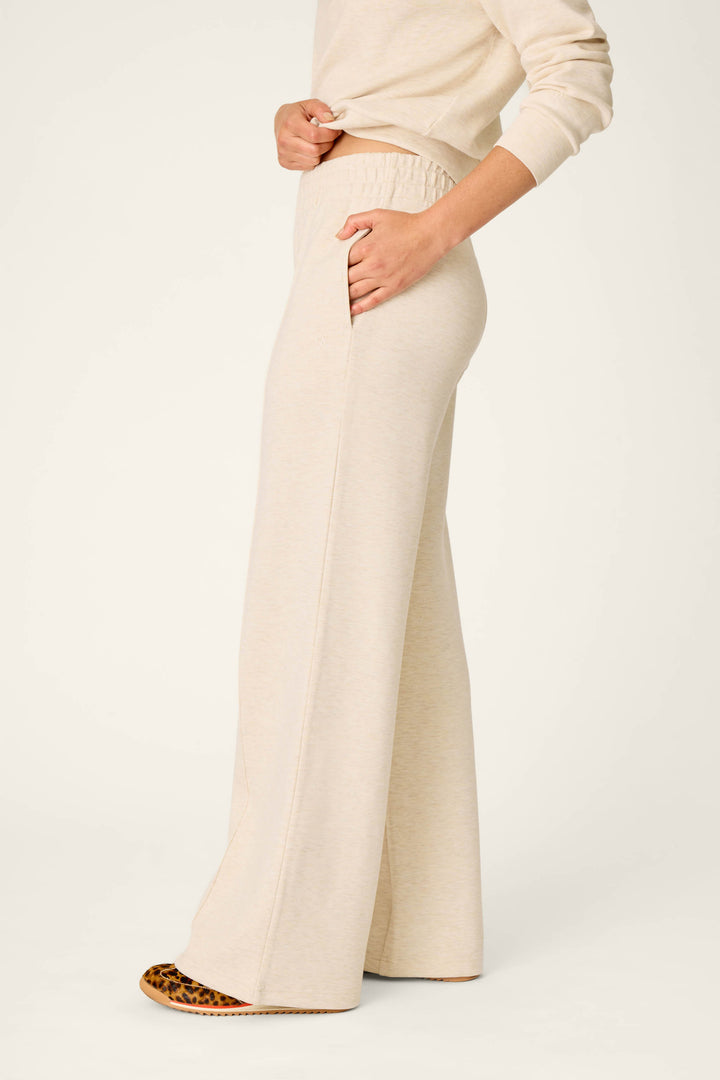 Wearing the P.J. Salvage Western Ways Good Luck Club Runway Lounge Pants, this person is shown from mid-chest down standing sideways. The beige, wide-leg, high-waisted lounge pants feature side pockets and reach the floor, with shoes partially visible beneath the hem.