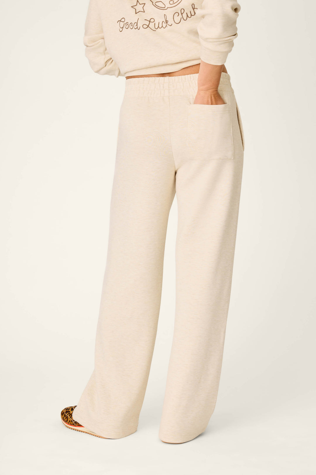 A person is shown from the waist down wearing the P.J. Salvage Western Ways Good Luck Club Runway Lounge Pants in a cream color, with one hand slipped into a side pocket. The pants are styled with a coordinating sweatshirt, set against a plain background.